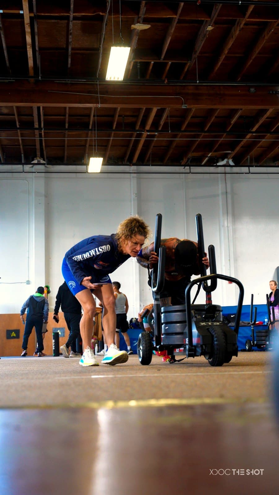 An athlete pushing the sled at a DEKA event while a coach cheers them on
